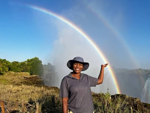 Woman smiling with a double rainbow at Victoria Falls in the background.